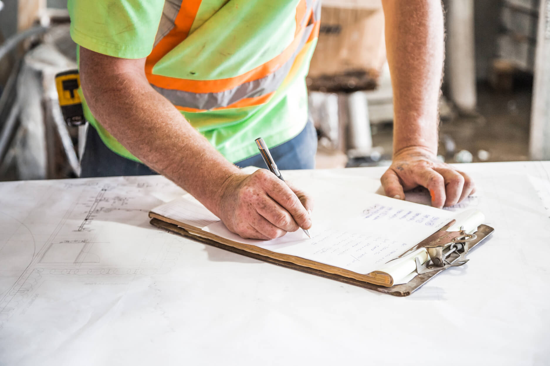 Person in high-visibility safety vest writing on a clipboard
