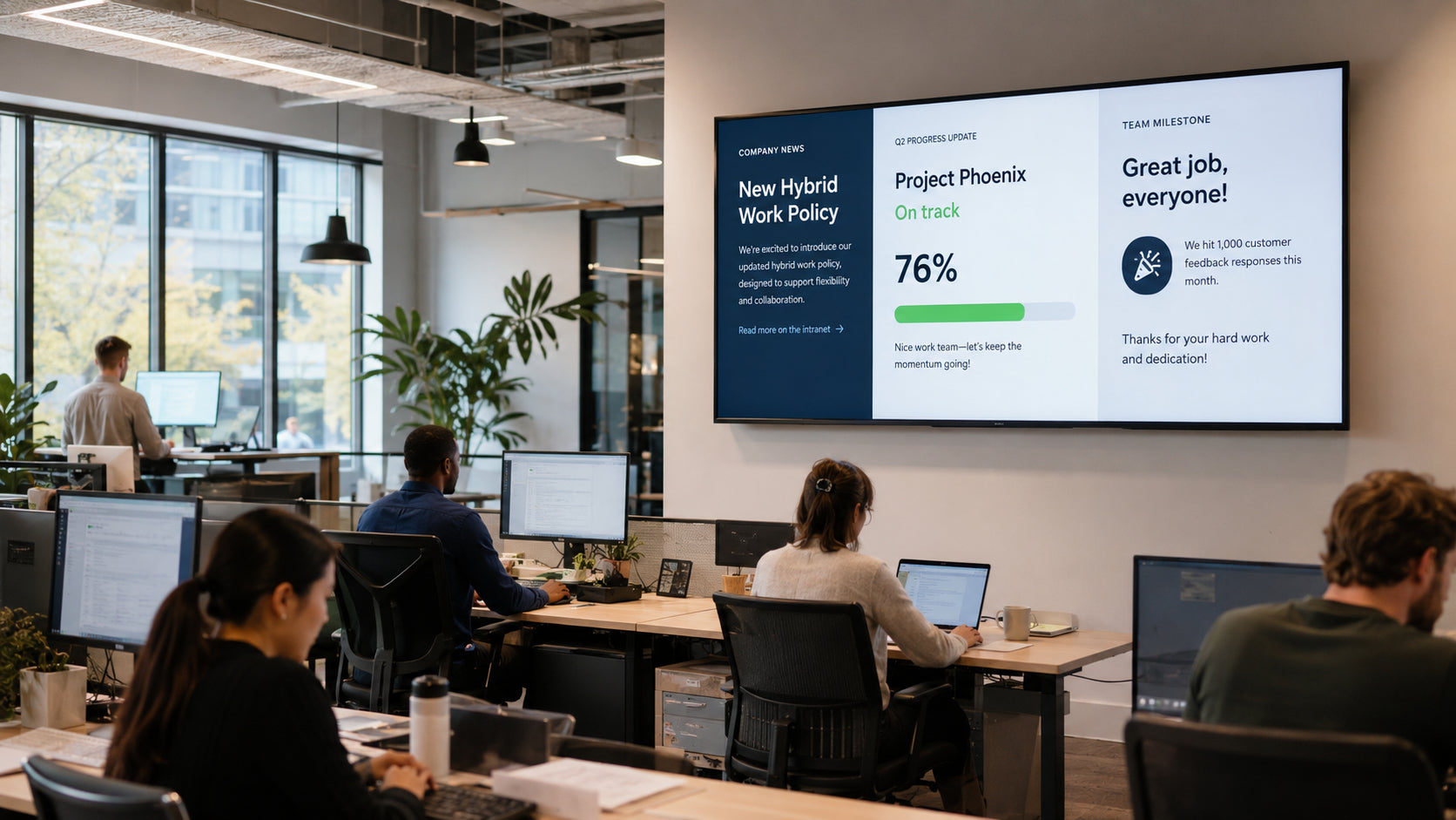 Modern office with employees working at desks, large screen displaying project information.