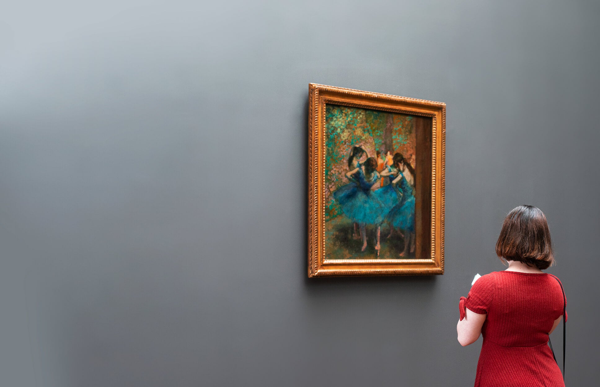 Woman in a red dress looking at a Degas painting