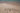 The word 'TRAVEL' written in sand on a beach with turquoise water in the background.